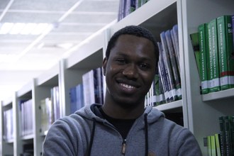 Em plano médio, foto mostra Bachelor sorrindo, com o fundo das prateleiras da biblioteca