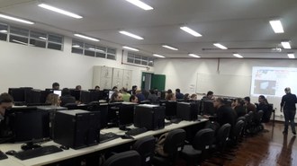 Sala com computadores dispostos em linha, e pessoas utilizando os equipamentos