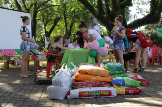 Pilha com ração para animais e ao fundo pessoas participando de arrecadação