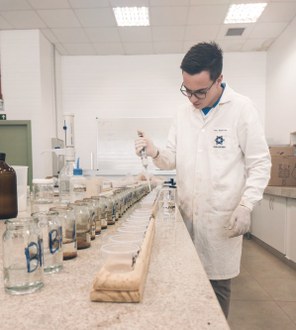 Estudante com jaleco branco, próximo a bancada de laboratório com amostras