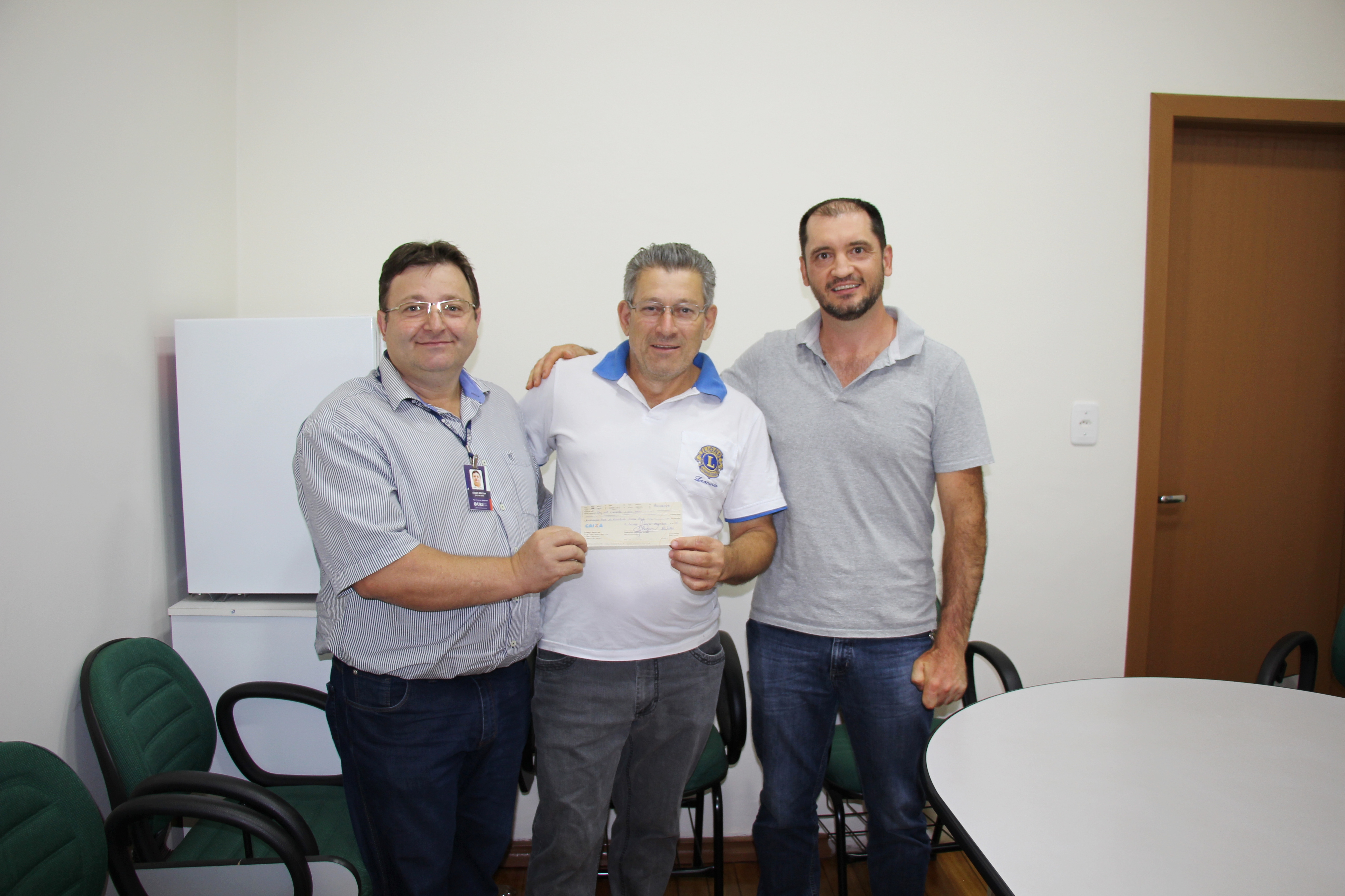 Em pé, três homens posam para foto segurando o cheque com o valor da doação