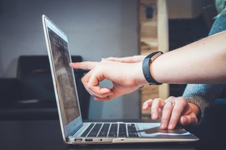 foto onde aparece um notebook e duas mãos apontando pra tela