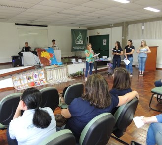 Quatro mulheres de pé, com uma delas ao microfone, falando para a plateia