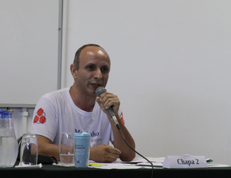 Na imagem o professor Martinho Machado Júnior está sentado e segurando microfone.