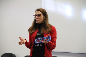 Na imagem a palestrante Maristela Vanin Pinto está no palco do auditório e faz demonstração usando o Sorobã, que está em sua mão esqueda.