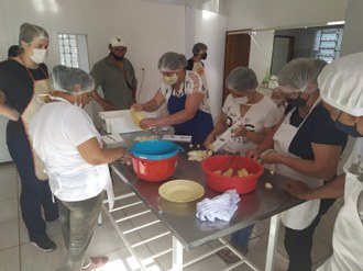 Fotografia retrata um grupo de pessoas ao redor de uma mesa. As pessoas estão manuseando e preparando alimentos. Foto: Julian Perez-Cassarino.