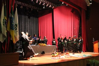 Foto do palco no final festivo da colação, onde caem serpentinas e formandos comemoram.