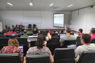 Professores sentados no auditório assistem apresentação.