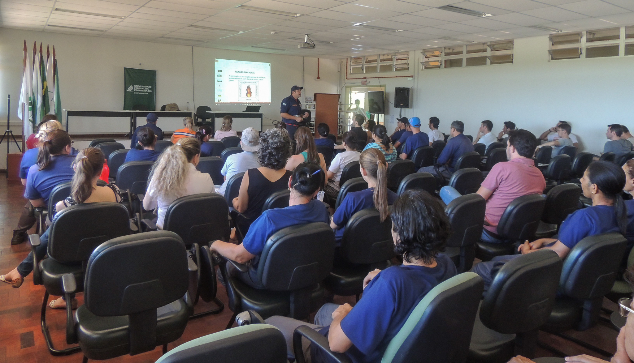 Ao fundo, homem ministrando curso para várias pessoas