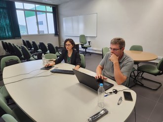 Foto de um homem e uma mulher sentados numa mesa olhando um computador