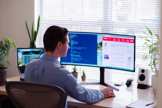 Um homem sentado de costas e na sua frente uma mesa de trabalho com um computador (imagem: unplash)