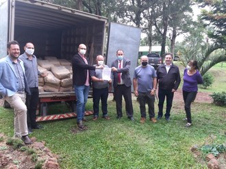 sete homens e uma mulher posam para foto na frente de um caminhão. A parte traseira do caminhão está aberta com vários sacos de farinha dentro