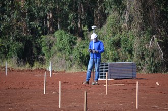 um homem de pé segura uma peça da usina fotovoltaica, atrás dele uma mata verde fechada.