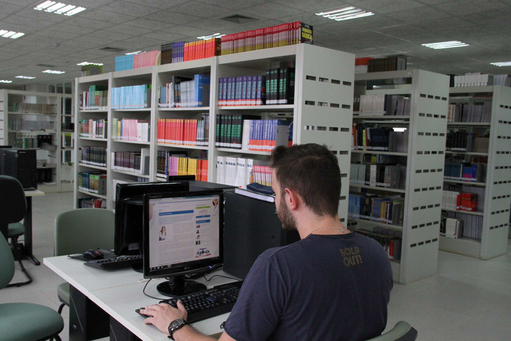 Aluno, na biblioteca da UFFS, sentado e olhando para uma tela de computador.