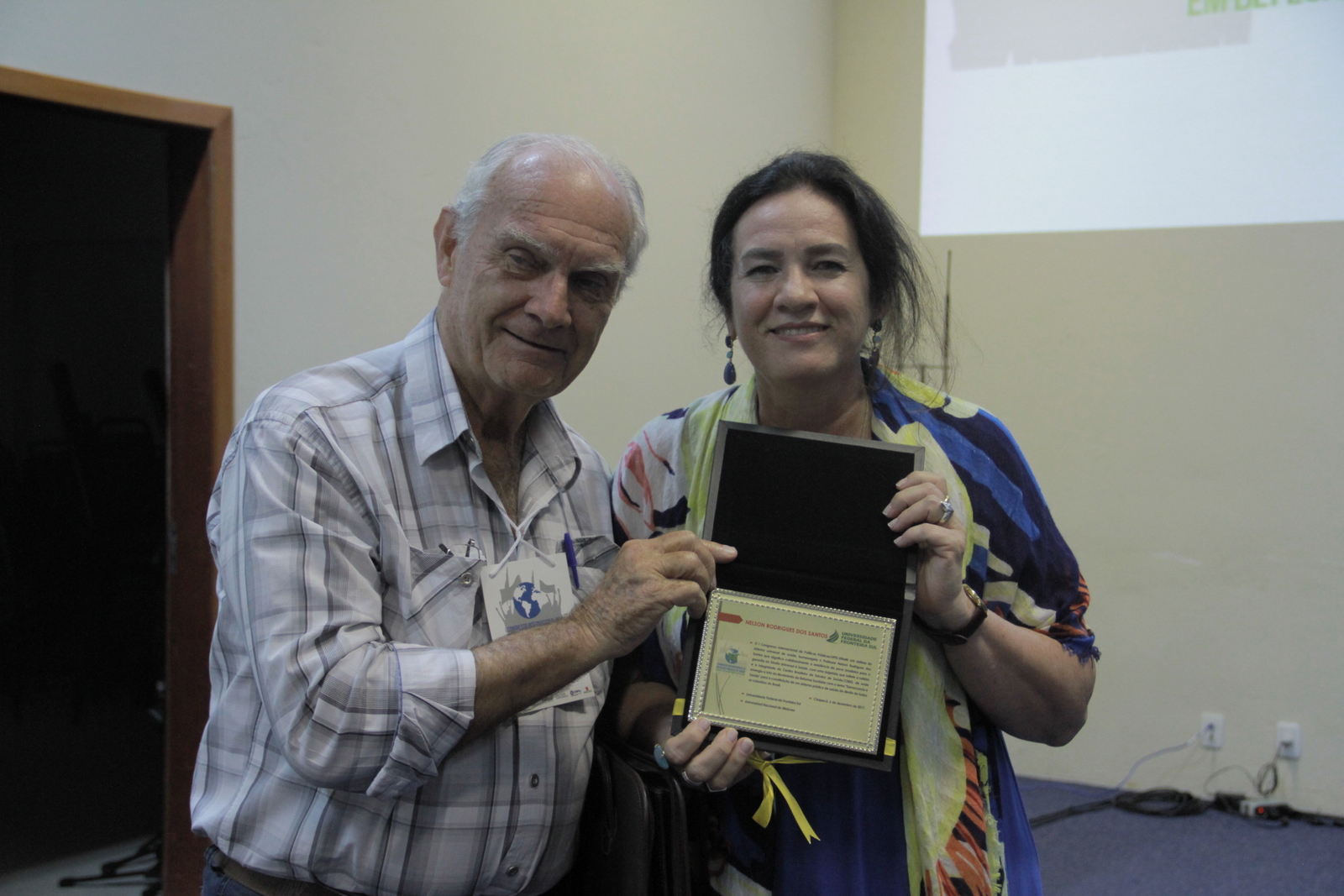 Um homem e uma mulher posam para uma foto segurando uma placa de homenagem